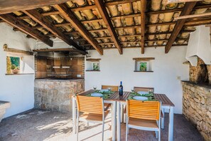 An outdoor dining area with a stone wall, wooden ceiling beams, and a built-in grill. - Hillside Villa With Pool for 5 (Pollença)