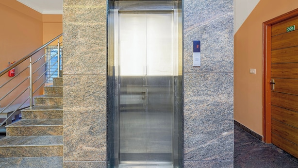 Un ascensor con pantalla digital, una escalera con barandillas de metal y una puerta de madera con placa de identificación.