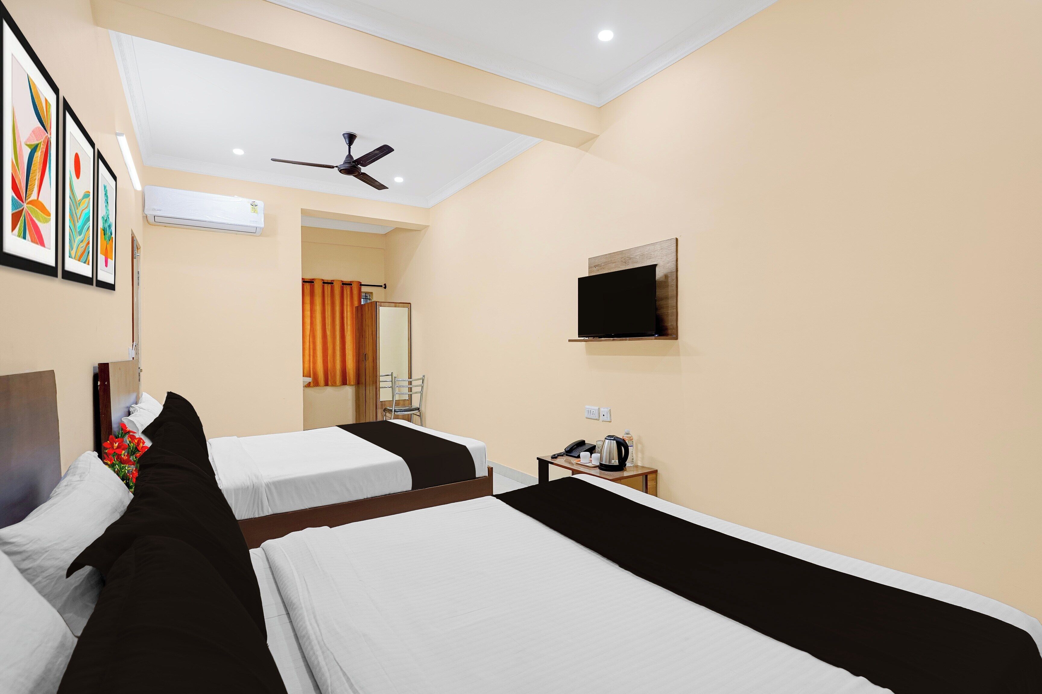 A hotel room with two beds, a ceiling fan, a flat-screen TV, and a small table with a kettle and cups.