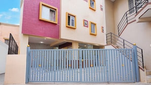 Un edificio de varios pisos con una verja azul, fachada rosa y beige, y una escalera a la derecha.