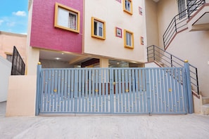 Un edificio de varios pisos con una verja azul, fachada rosa y beige, y una escalera a la derecha.