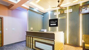 Un mostrador de recepción con un letrero que indica servicio de la empresa, un ventilador de techo y una zona de espera con una silla.