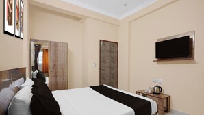 Habitación de hotel con cama, televisor montado en la pared, armario de madera y una mesita con hervidor y tazas.