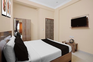 Habitación de hotel con cama, televisor montado en la pared, armario de madera y una mesita con hervidor y tazas.