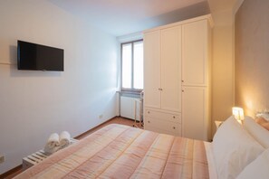 Ein Schlafzimmer mit einem Bett, einem an der Wand montierten Fernseher, einem Kleiderschrank und einem Fenster.