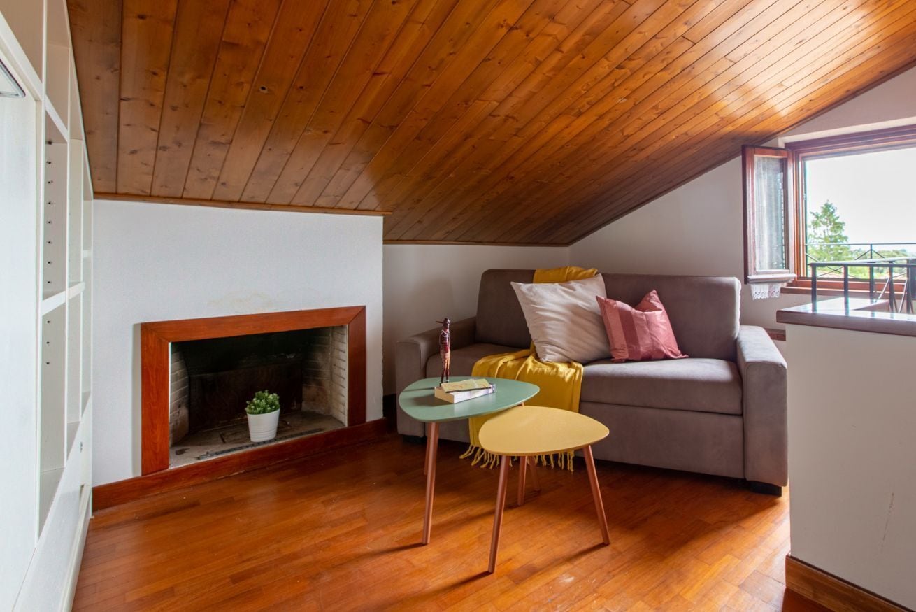 Um quarto acolhedor com teto de madeira, lareira, sofá e uma mesinha.