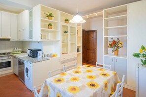 Eine kompakte Küche mit Waschmaschine, einem Esstisch mit Sonnenblumen-Tischdecke und eingebauten Regalen mit Topfpflanzen.