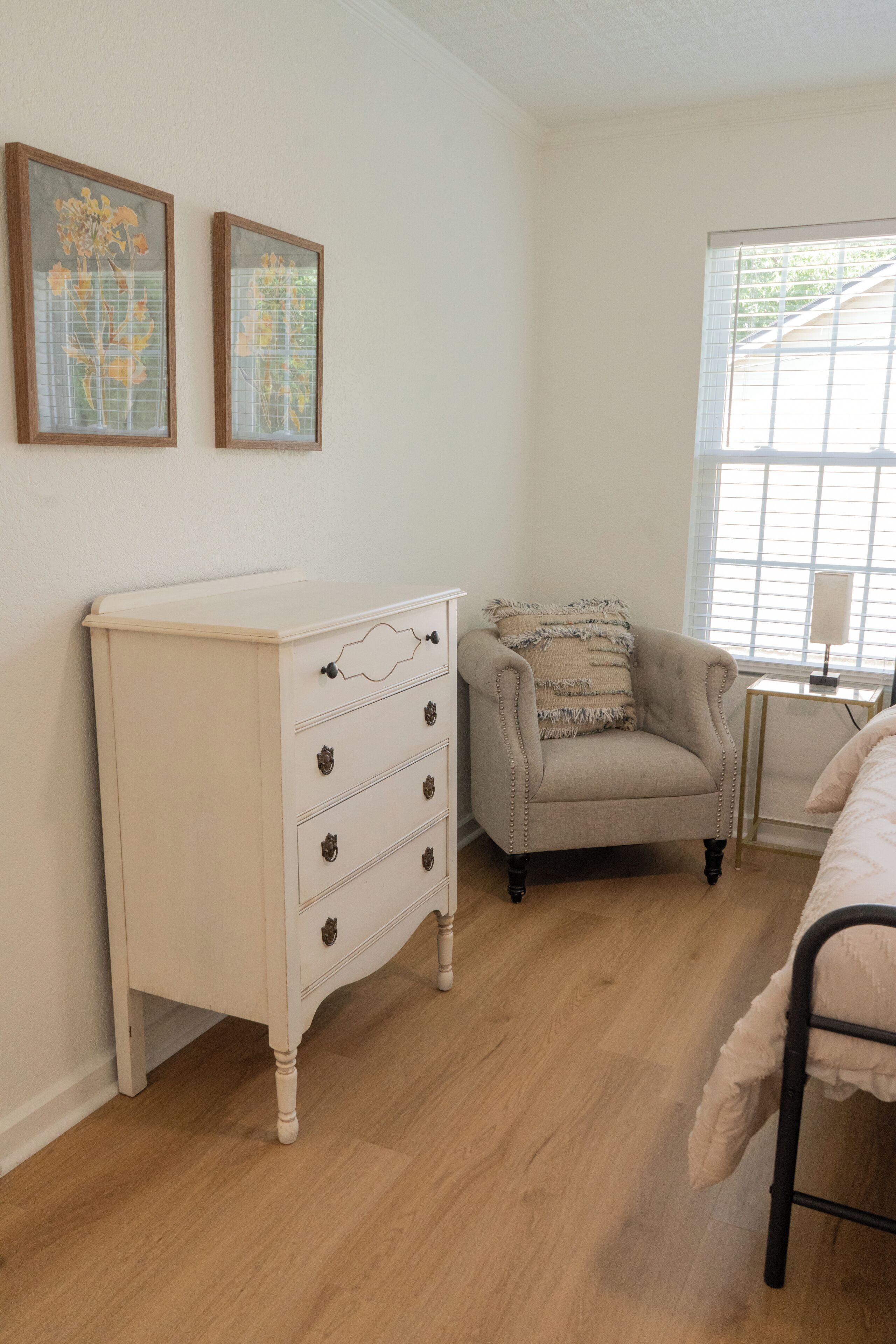 A room with a white dresser, a beige armchair, and a window with blinds.