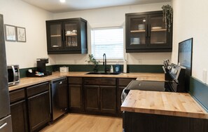 Una cocina con gabinetes de madera oscura, lavavajillas empotrado, microondas y encimera de madera.