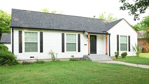 A single-story house with a dark roof, white siding, and a front porch with a door and windows. - This home located in the Temple Historic District has recently been renovated and updated for a luxurious stay, while maintaining the aesthetic historical  vibe. (TEMPLE)