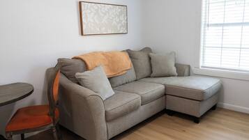 A sectional sofa with a throw blanket, a wooden chair, and a framed artwork on the wall.