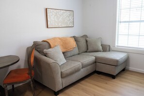 A sectional sofa with a throw blanket, a wooden chair, and a framed artwork on the wall.