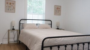 Ein Schlafzimmer mit einem Bett, Nachttischen, einem Fenster mit Jalousien und Wandbildern.