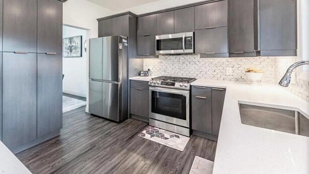 A modern kitchen with dark cabinetry, stainless steel appliances, and a white backsplash.