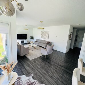 A modern living room with a sectional sofa, a flat-screen TV, and a dining area with a table and chairs.