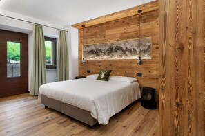 A bedroom with a wooden headboard, a bed with white bedding, a green pillow, a framed picture on the wall, and a window with curtains.