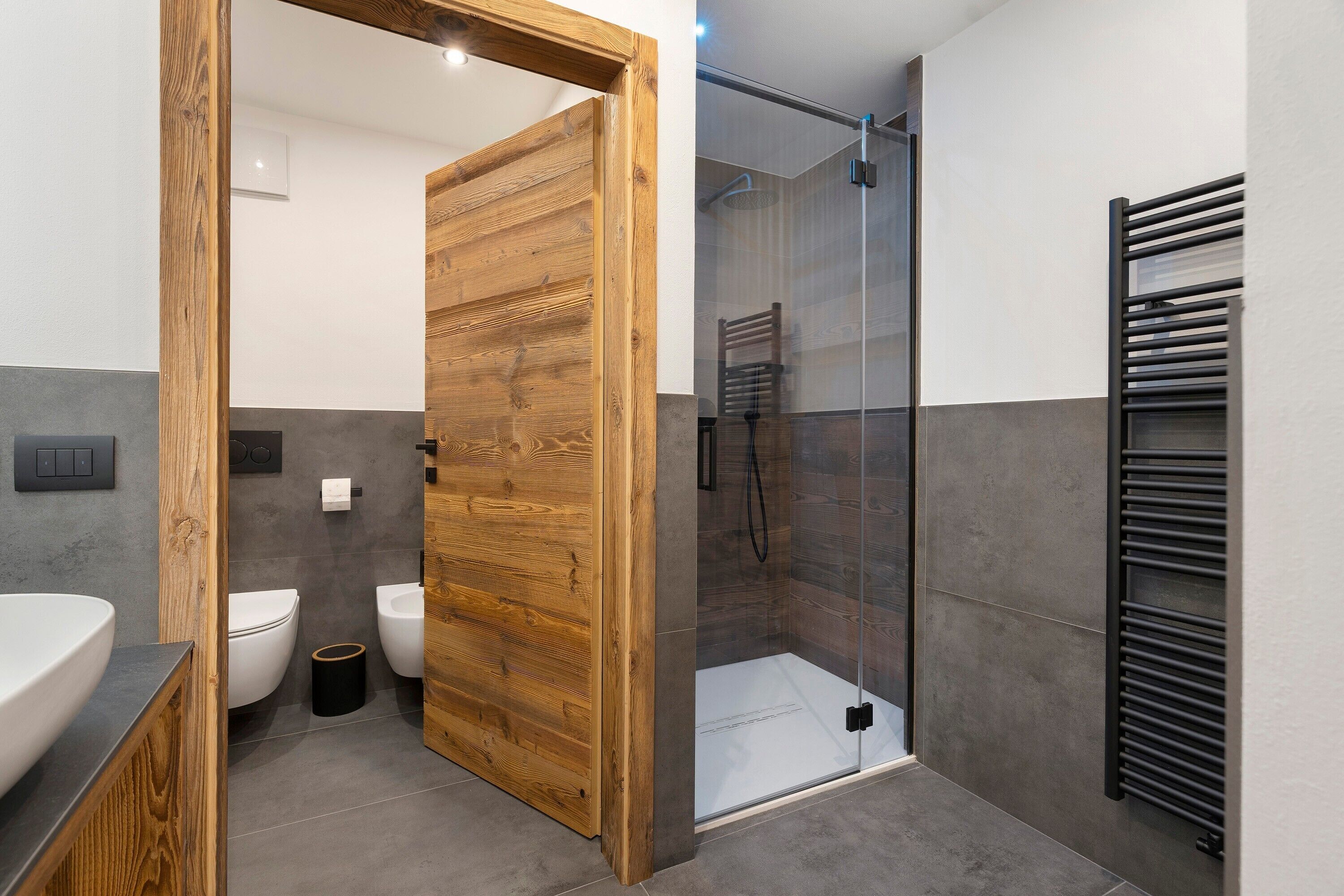 Une salle de bain moderne avec une porte en bois, une douche en verre et un porte-serviettes noir.
