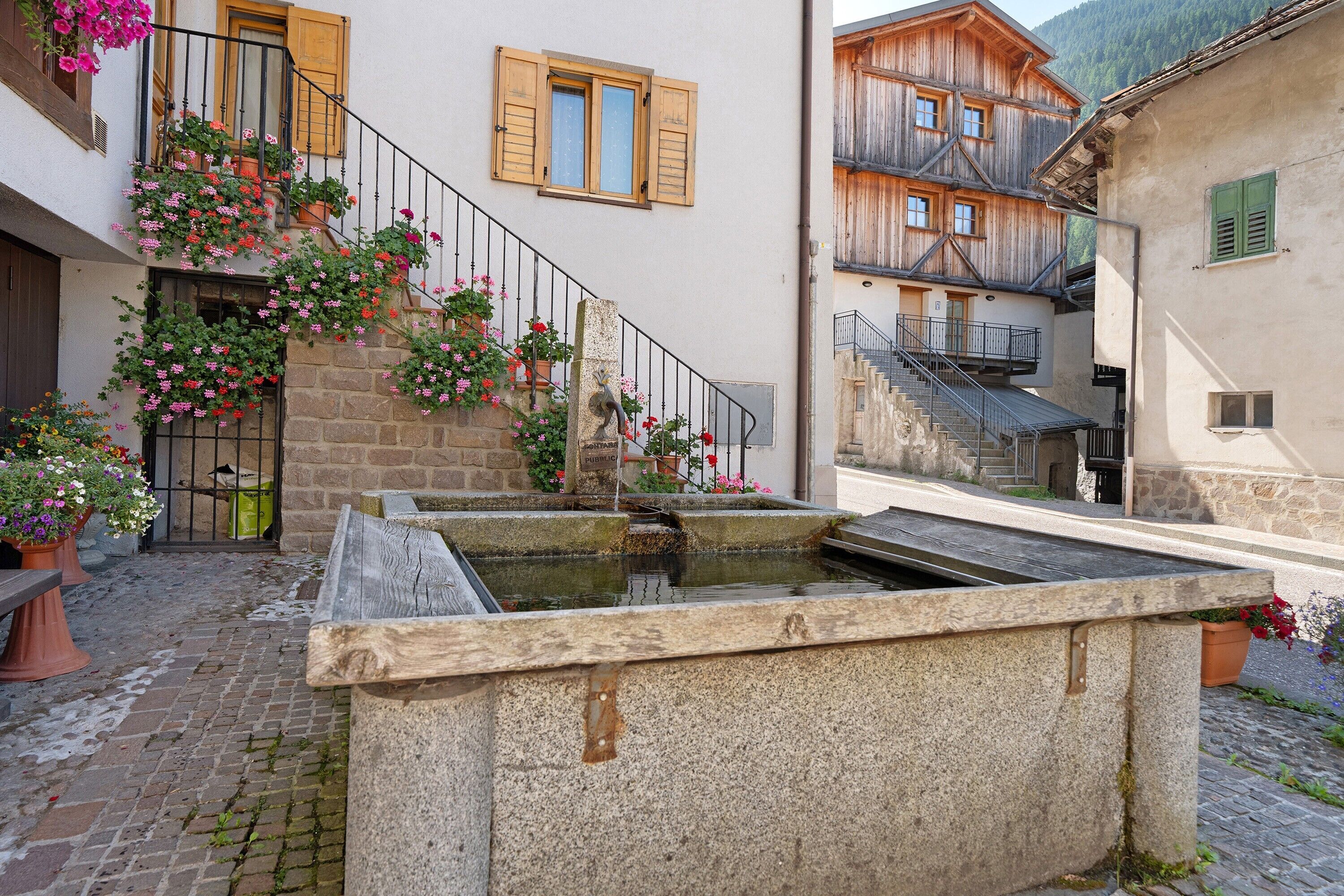 Un cortile con una fontana in pietra, piante in vaso e una scala che conduce a un edificio in legno.