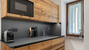 Een functionele keuken met een magnetron, koffiezetapparaat, spoelbak en houten kastjes.
