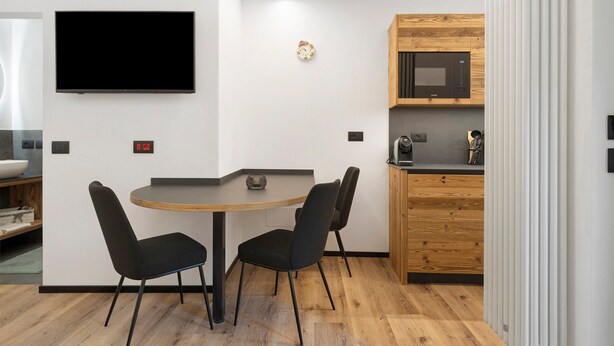 Een moderne keuken met een magnetron, een klok en een ronde tafel met stoelen.