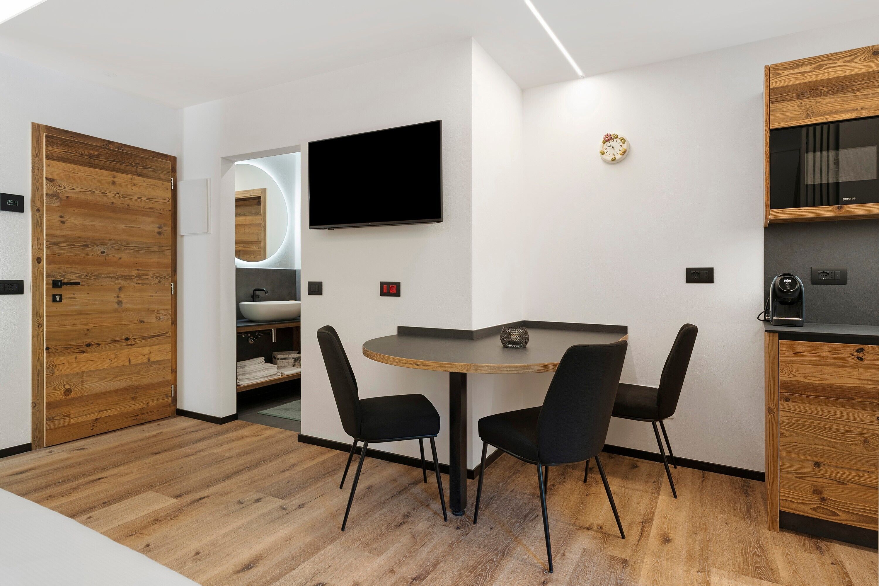 Une cuisine moderne avec des meubles en bois, une table ronde et deux chaises, un téléviseur à écran plat et un four encastré.