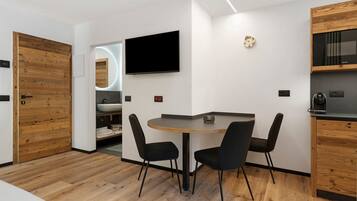 Une cuisine moderne avec des meubles en bois, une table ronde et deux chaises, un téléviseur à écran plat et un four encastré.