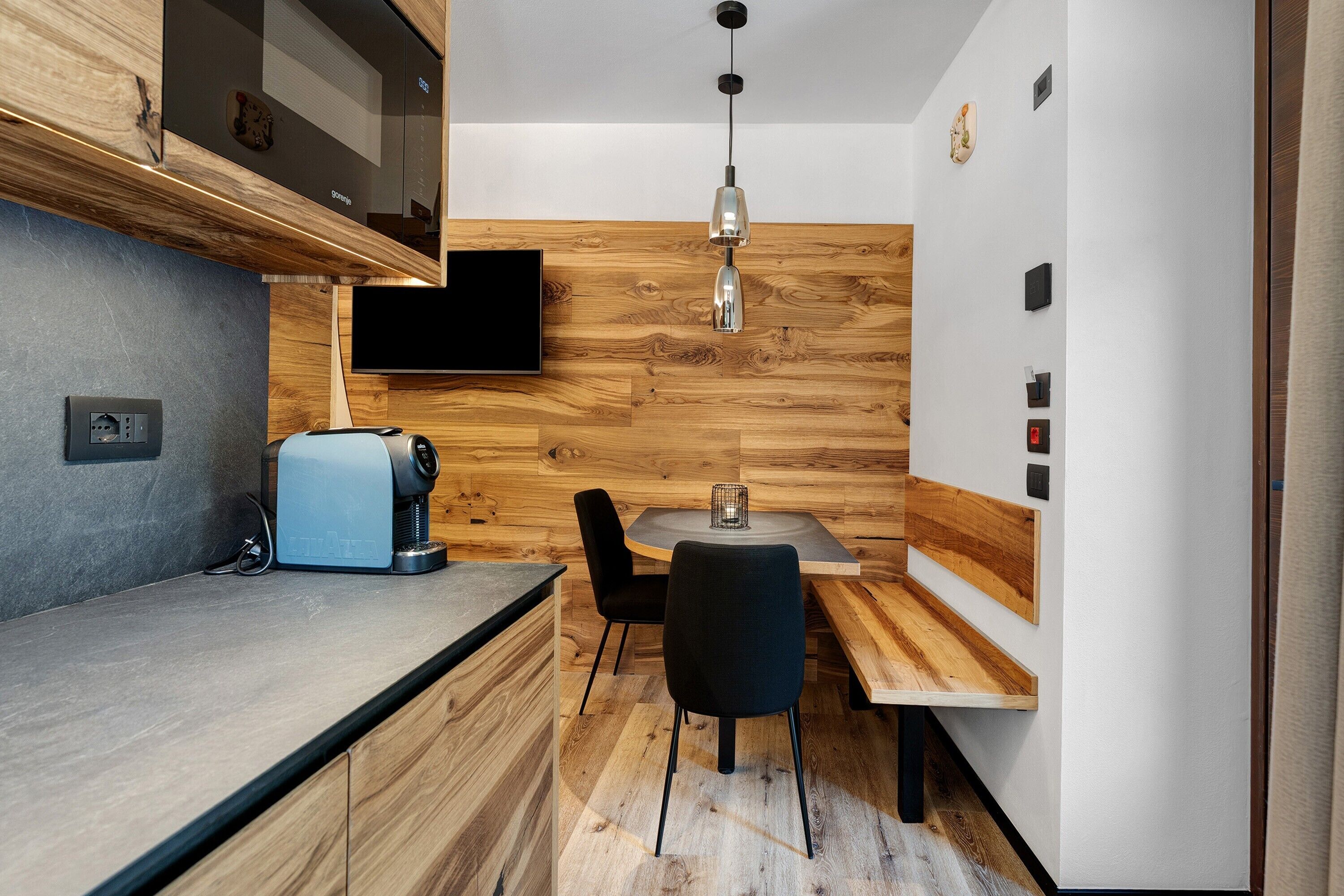 Una cocina compacta con horno integrado, cafetera, televisor de pantalla plana y comedor con mesa y sillas.