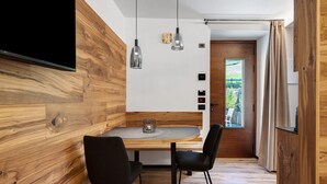 Et moderne spiseområde med en trævæg, et rundt bord, to stole, hængende lamper og udsigt gennem en dør.