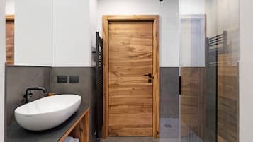 Un bagno moderno con una porta in legno, un lavabo a incasso bianco, un portasciuga e una cabina doccia in vetro.