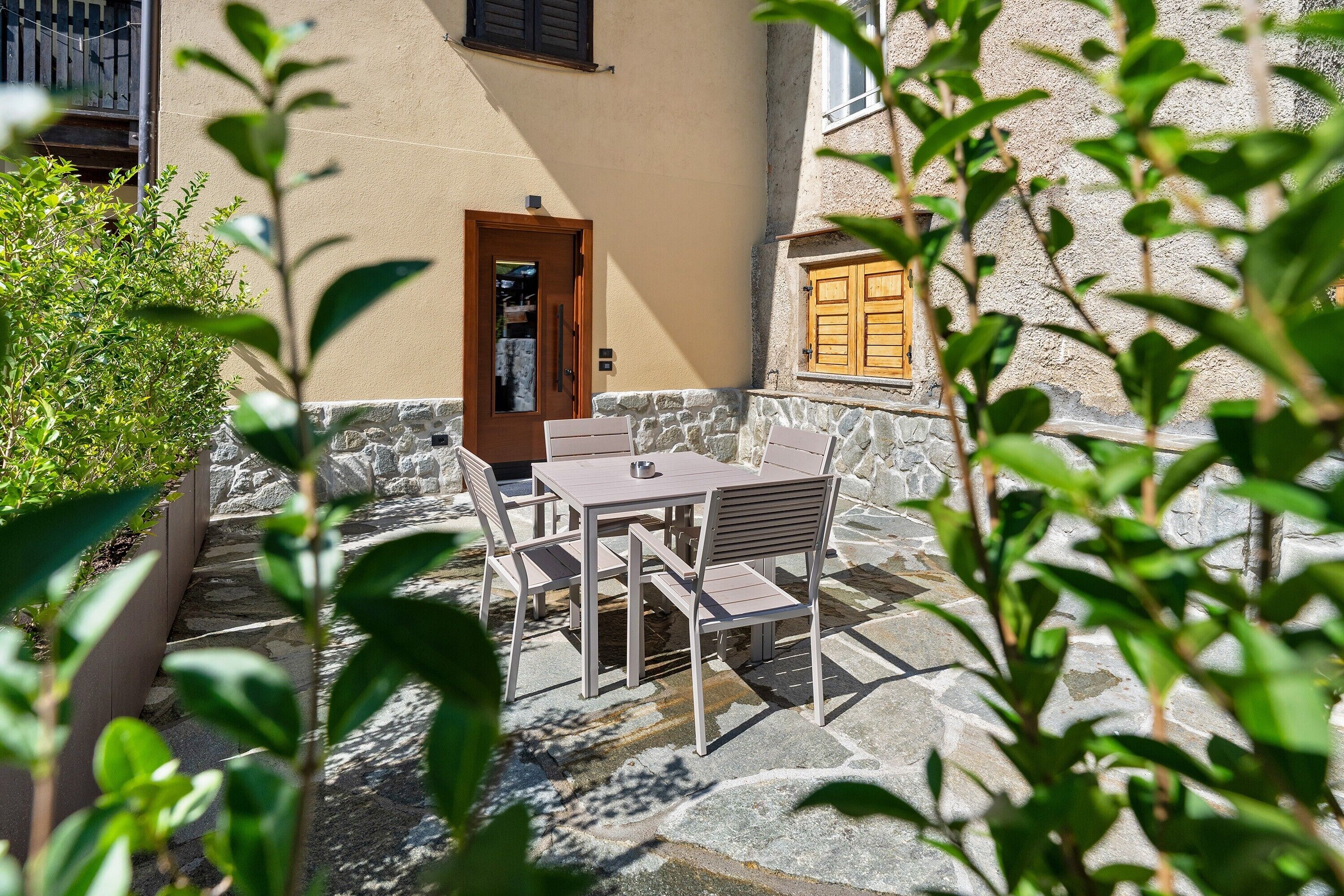 A patio with a table and chairs, a door, and a window with shutters.