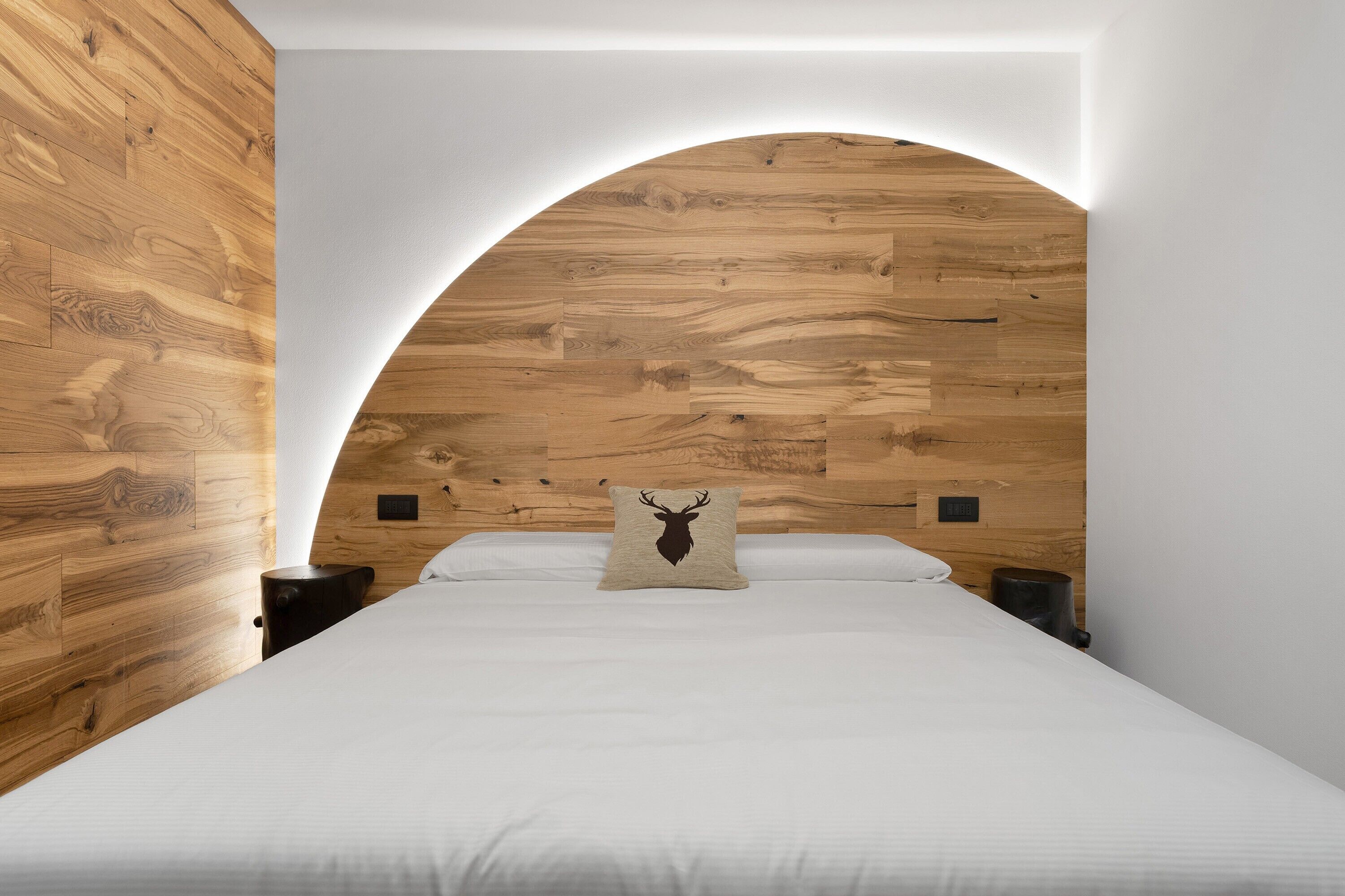 Une chambre à coucher avec une tête de lit en bois, un lit recouvert de linge de lit blanc et un oreiller orné de la silhouette d’un cerf.