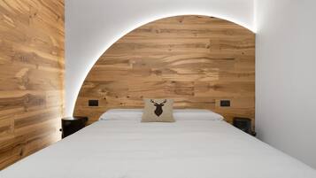 Une chambre à coucher avec une tête de lit en bois, un lit recouvert de linge de lit blanc et un oreiller orné de la silhouette d’un cerf.