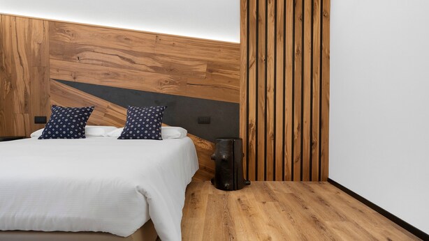 Un dormitorio moderno con cabecera de madera, cama con ropa blanca y mesita de noche con un objeto negro.