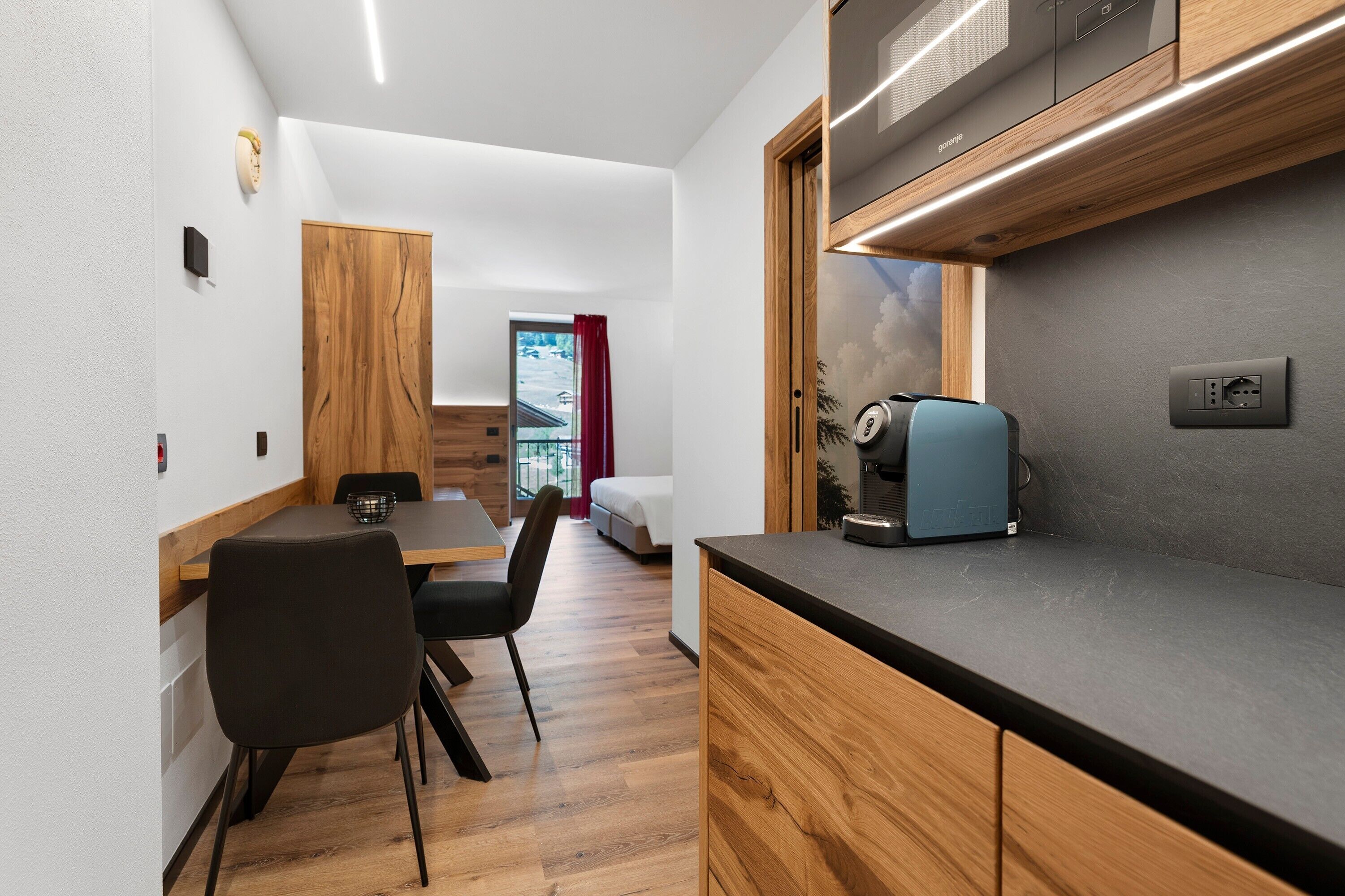 A modern kitchen with a coffee machine, wooden cabinets, and a dining area with a table and chairs.