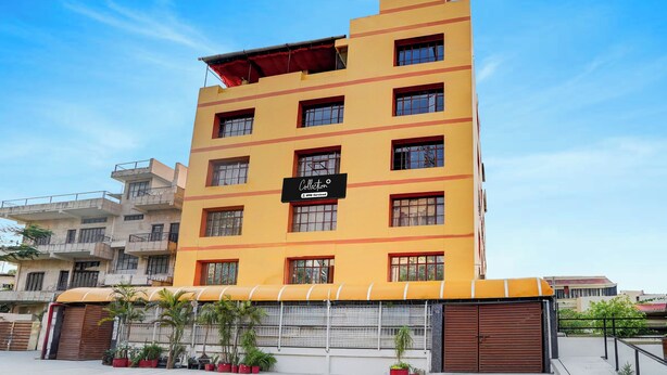 Edificio de varios pisos con fachada amarilla, un letrero que indica que es administrado por OYO, y una entrada con portones y plantas en macetas.