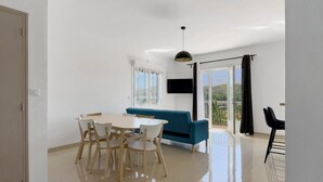 Ein modernes Wohnzimmer mit Essbereich, einer Couch, einem Fernseher und einem Balkon mit Blick.