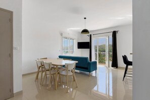 Ein modernes Wohnzimmer mit Essbereich, einer Couch, einem Fernseher und einem Balkon mit Blick.