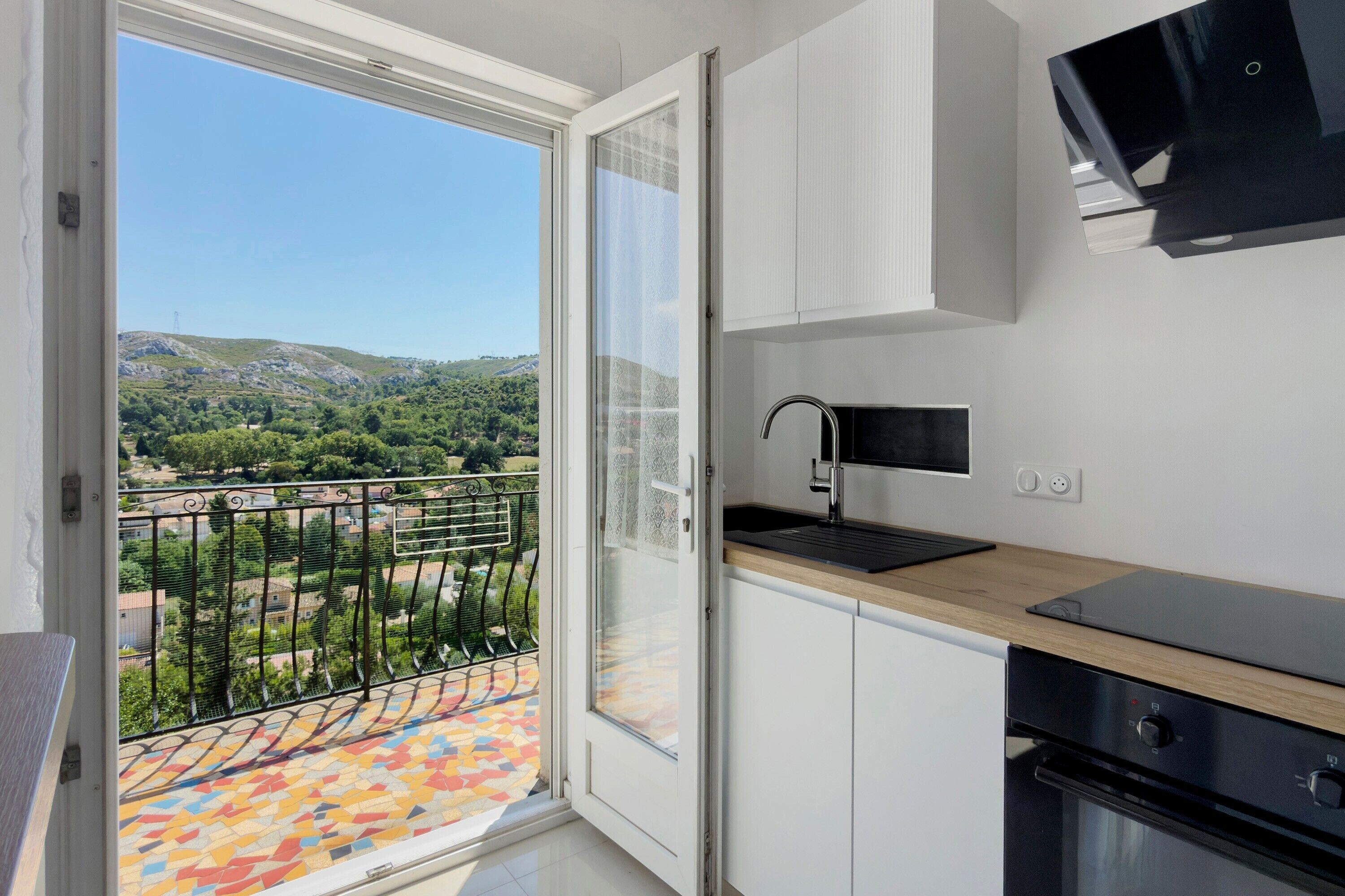 Een moderne keuken met uitzicht op een balkon en een bergachtig landschap.