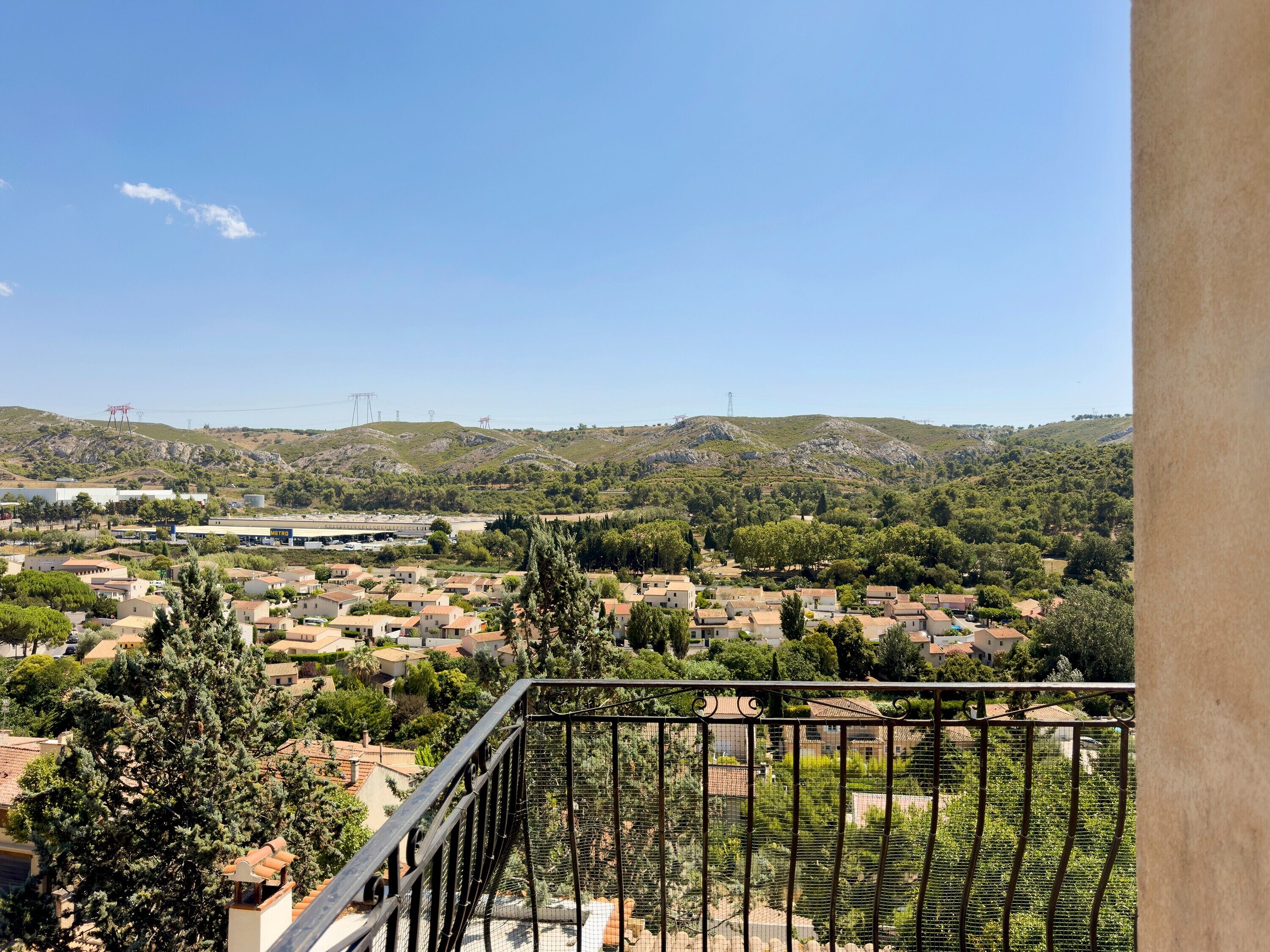 A balcony with a view of a residential area, a gas station, and hills in the distance.