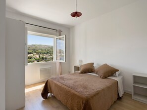 Une chambre à coucher avec un lit, une table de chevet, une lampe et une vue sur la ville par la fenêtre.