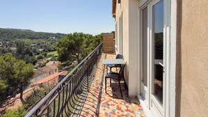 Ein Balkon mit Fliesenboden, einem Tisch mit Stühlen und Blick auf eine hügelige Landschaft.
