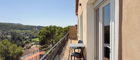 Un balcon doté d’un sol carrelé, d’une table avec des chaises et offrant une vue sur un paysage vallonné.