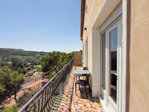 Ein Balkon mit Fliesenboden, einem Tisch mit Stühlen und Blick auf eine hügelige Landschaft.