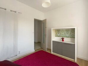 Ein Zimmer mit rotem Teppich, einem weißen Kleiderschrank, einer grauen Kommode und einer Tür zu einem anderen Raum.
