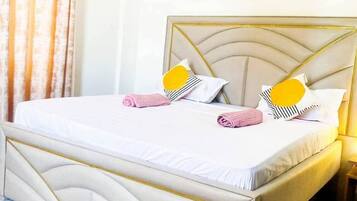 Una cama bien hecha con cabecera, aire acondicionado de pared y cuadros colgados encima.