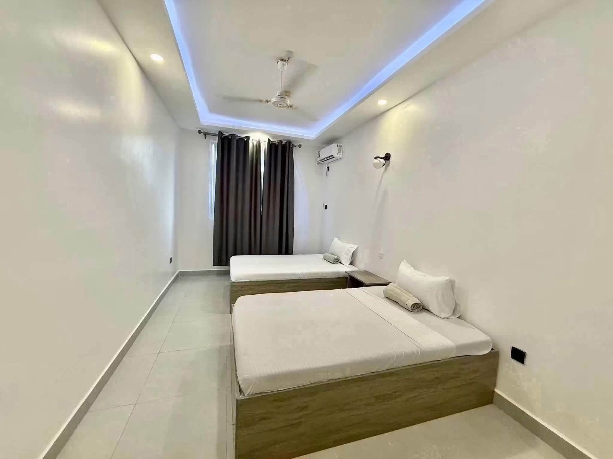 A modern hotel room with two beds, a ceiling fan, and an air conditioning unit.
