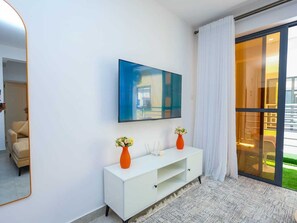 Una habitación de hotel moderna con una mesa consola blanca, dos jarrones naranjas con flores, un cuadro azul grande y una puerta corrediza de vidrio a un balcón.