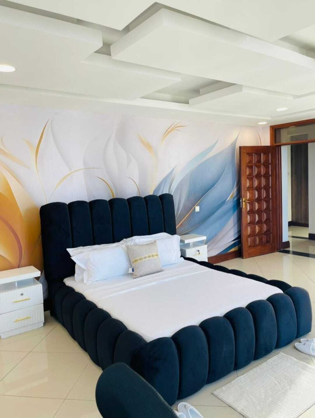 A modern bedroom with a large bed, a nightstand, a wooden door, and a decorative wall mural.