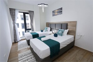 Una habitación de hotel con dos camas, un ventanal grande, un cuadro en la pared y una lámpara en el techo.
