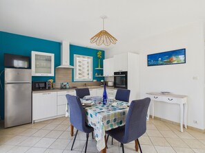 A compact kitchen with white cabinets, a microwave, a stove, and a dining table set for four. - House and garden for 3 near the beach (La Plaine-sur-Mer)
